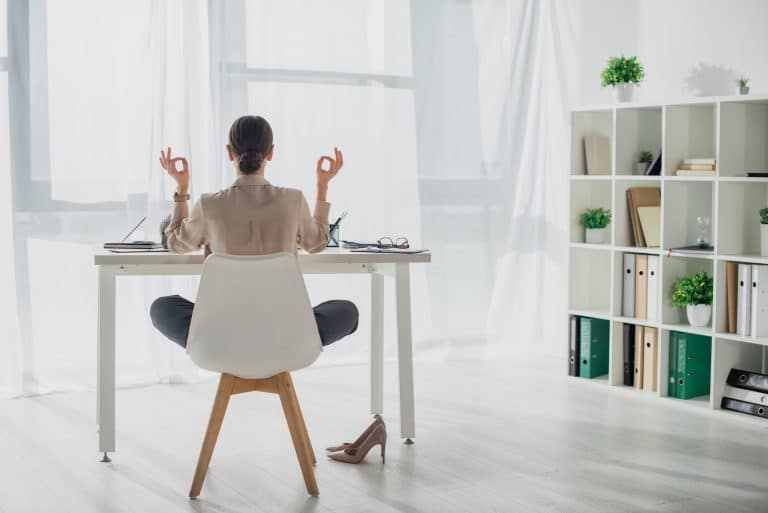 Back view of businesswoman meditating in lotus pose with gyan mudra at workplace