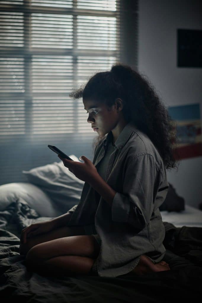 Stressed youthful girl in grey shirt sitting on her knees on double bed