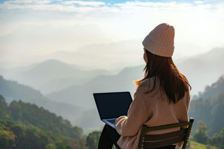 Young woman freelancer working online using laptop and enjoying the beautiful nature landscape